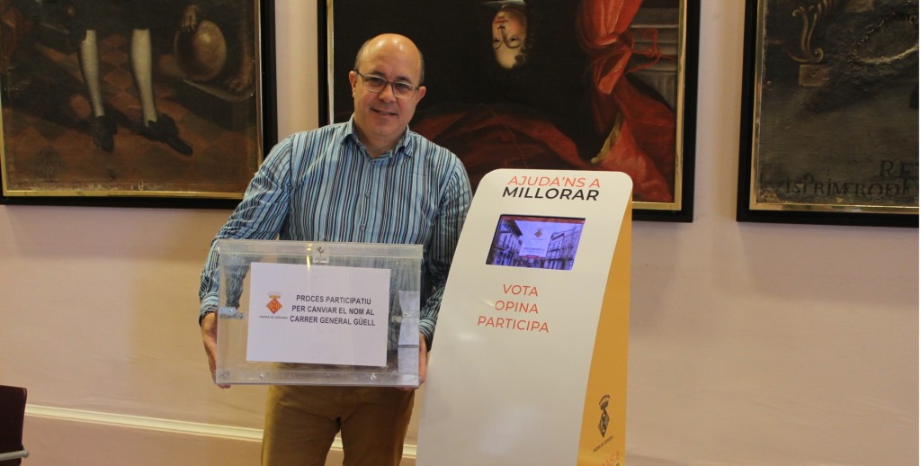 Imatge de l'alcalde de Cervera, Ramon Royes, sostenint una urna, al costat del dispositiu tàctil instal·lat al vestíbul de la Paeria perquè els veïns puguin presentar les seves propostes, el 24 de gener del 2019. (Horitzontal)