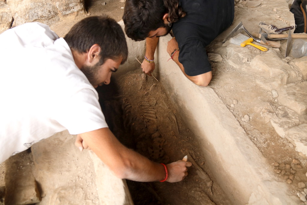 Pla mitjà on es poden veure dos arqueòlegs netejant les restes del cos de l'època tardo-romana que s'ha localitzat a la Iesso de Guissona, el 17 de juliol de 2019. (Hortizontal)